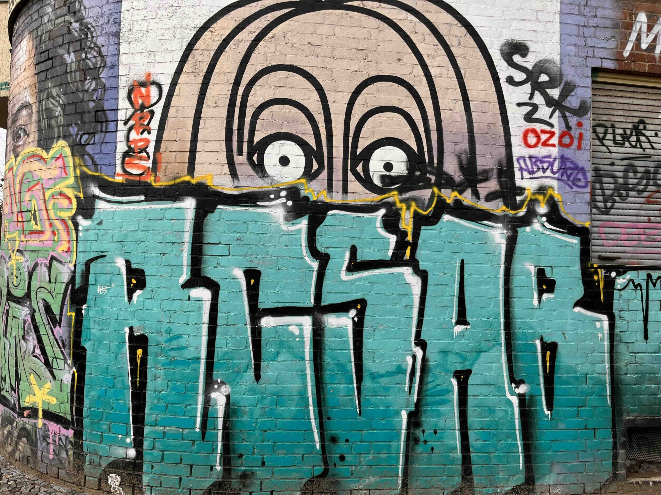 Graffiti of a mint green tag that says ACSAR and the image of a face peeking over it