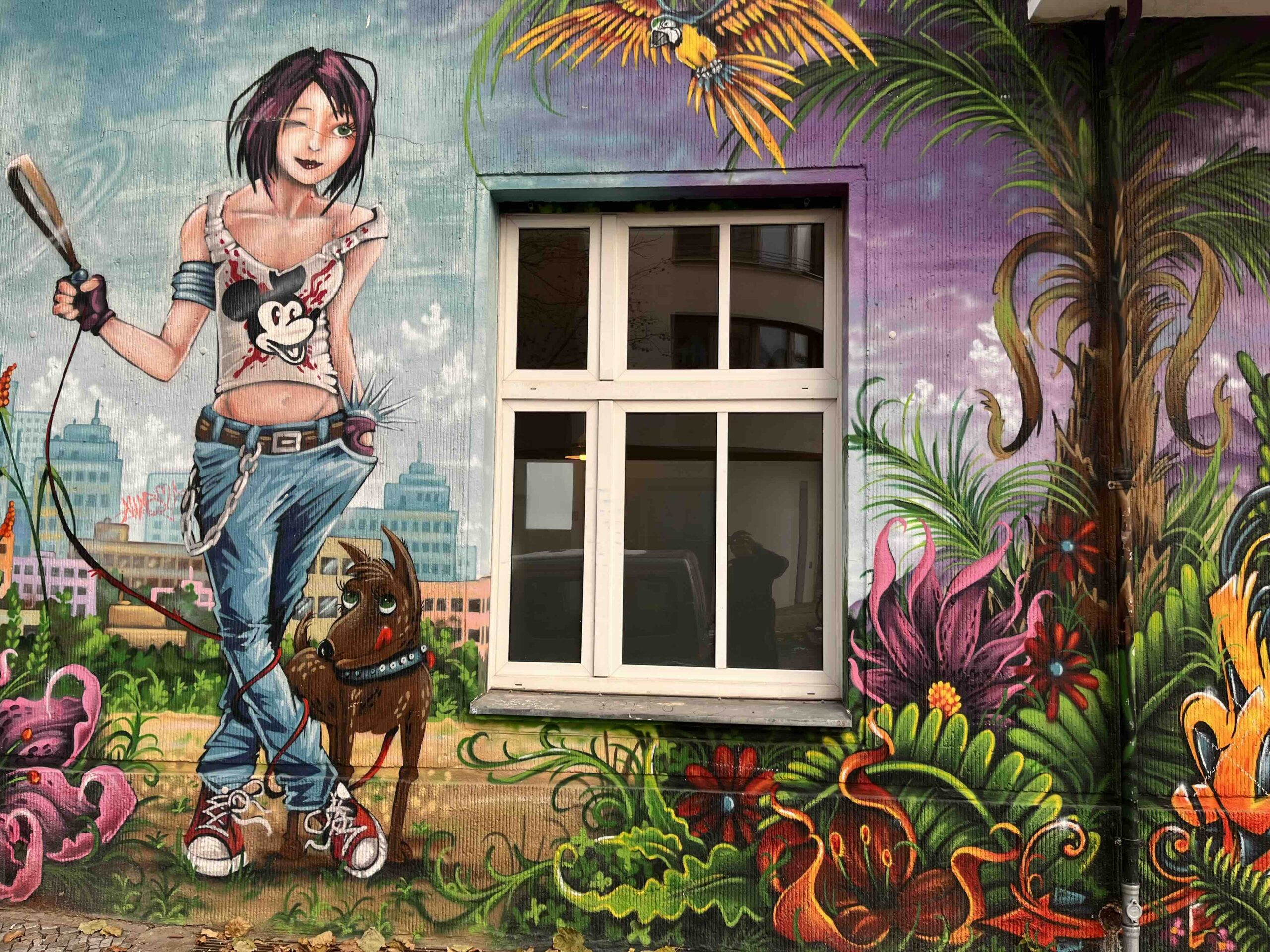 Graffiti of a young woman with a mickey mouse tank on standing in a field of flowers. She has a dog with her.